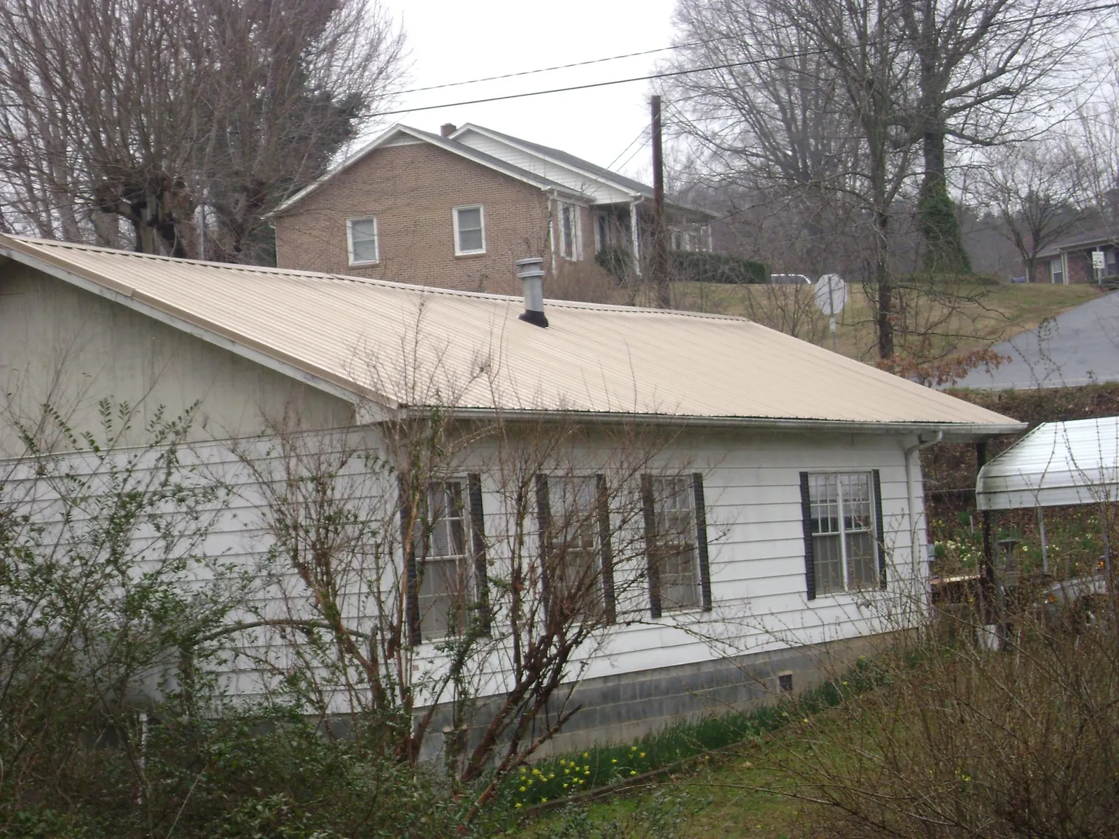 Tan metal roof on a white sided house set into a hillside — Commercial Roofing by Roofing Brothers in Avondale